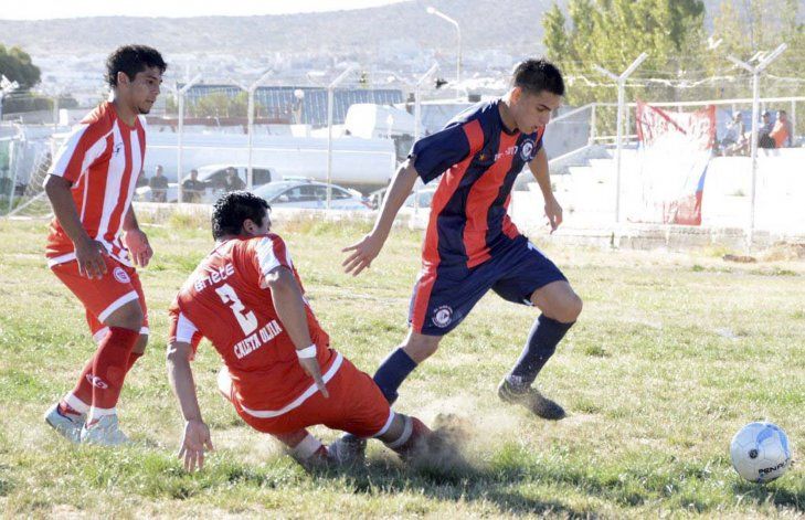 Enzo Bertoldi intenta eludir a José Vázquez y también a los yuyos del estadio Juan Domingo Perón.